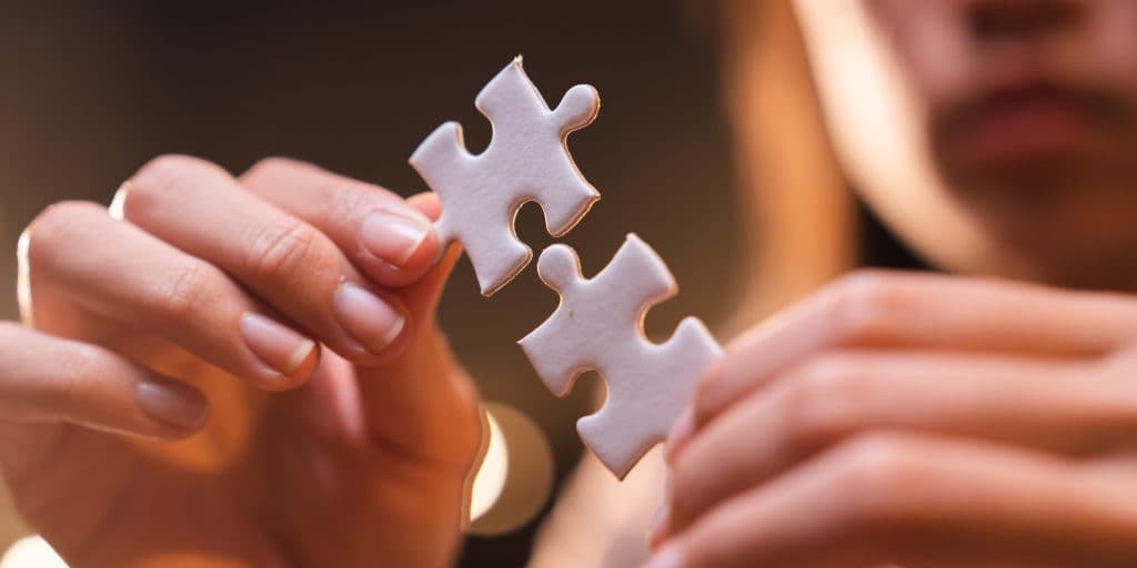 Person mit Fokus auf den Händen, die jeweils ein Puzzleteil halten, die ineinander passen.