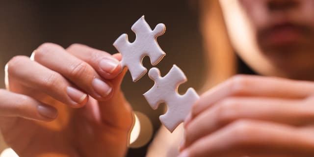 Person mit Fokus auf den Händen, die jeweils ein Puzzleteil halten, die ineinander passen.