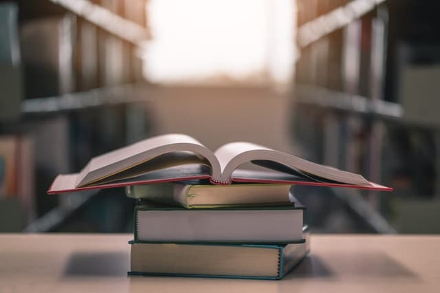 Vier Bücher liegen gestapelt auf einem Tisch, das oberste Buch ist aufgeklappt.
