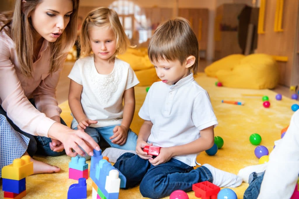 Erzieherin spielt mit Kindern in einer Kita. Vor ihnen liegen Bauklötze.