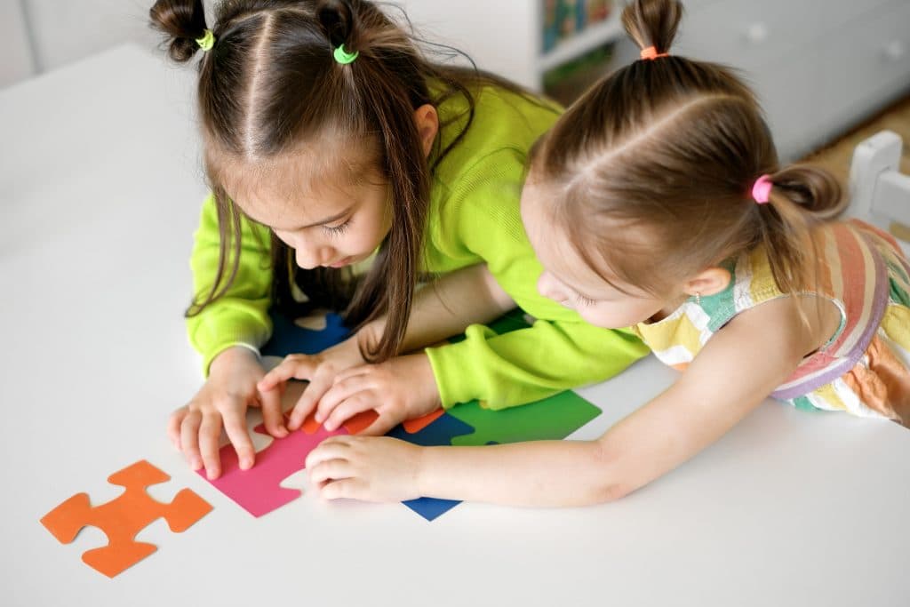 Zwei Mädchen beugen sich über den Tisch und setzen gemeinsam ein buntes Puzzle zusammen.