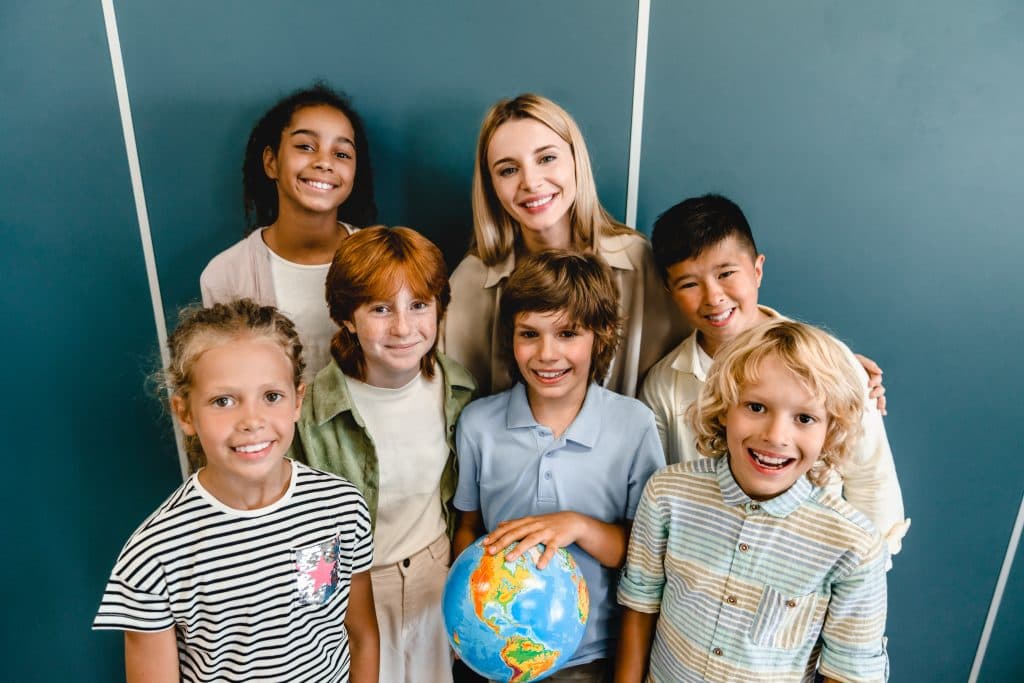 Pädagogische Fachkraft mit einer Gruppe fröhlicher Kinder, eines hält einen Globus.