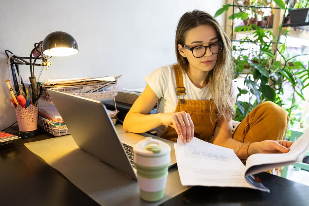 Eine Kita-Leitung mit langen Haaren und Brille sitzt im Büro am Schreibtisch und geht Unterlagen durch.