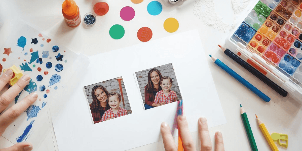 Auf einem hellen Arbeitsplatz verzieren Hände ein weißes Blatt Papier mit Fotos mithilfe von bunten Farben, Stiften und Bastelmaterialien.