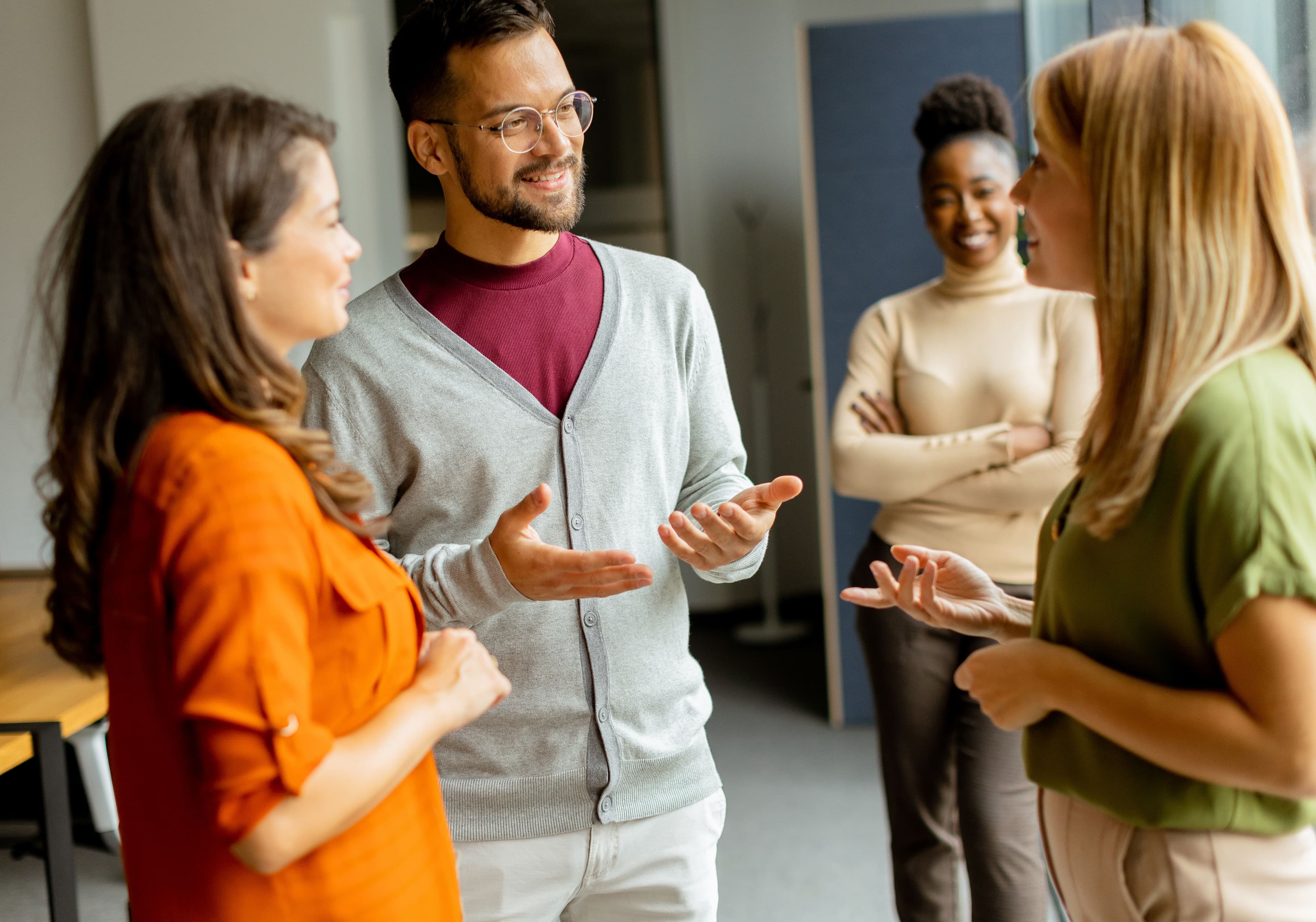 Vier Personen unterhalten sich lebhaft in einem Büro, wobei ein Mann gestikuliert und drei Frauen aufmerksam zuhören.