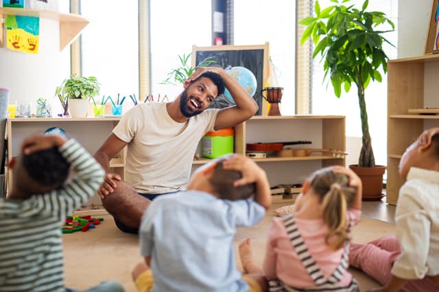 Erzieher macht Dehnübungen mit Kindern in der Kita.