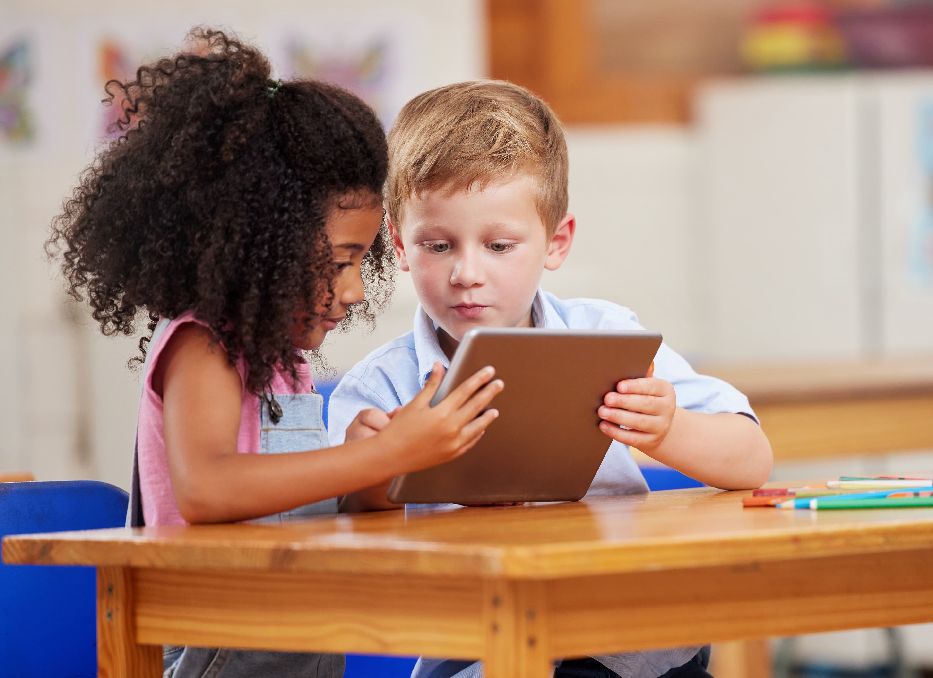 Ein Mädchen und ein Junge sitzen im Kindergarten an einem Tisch und schauen auf ein iPad.