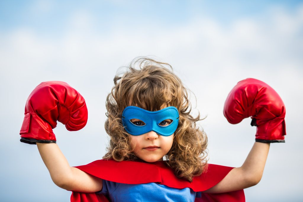 Kind im Superhelden Anzug verdeutlicht den systemrelevanten Beruf von Erziehern und pädagogischen Fachkräften