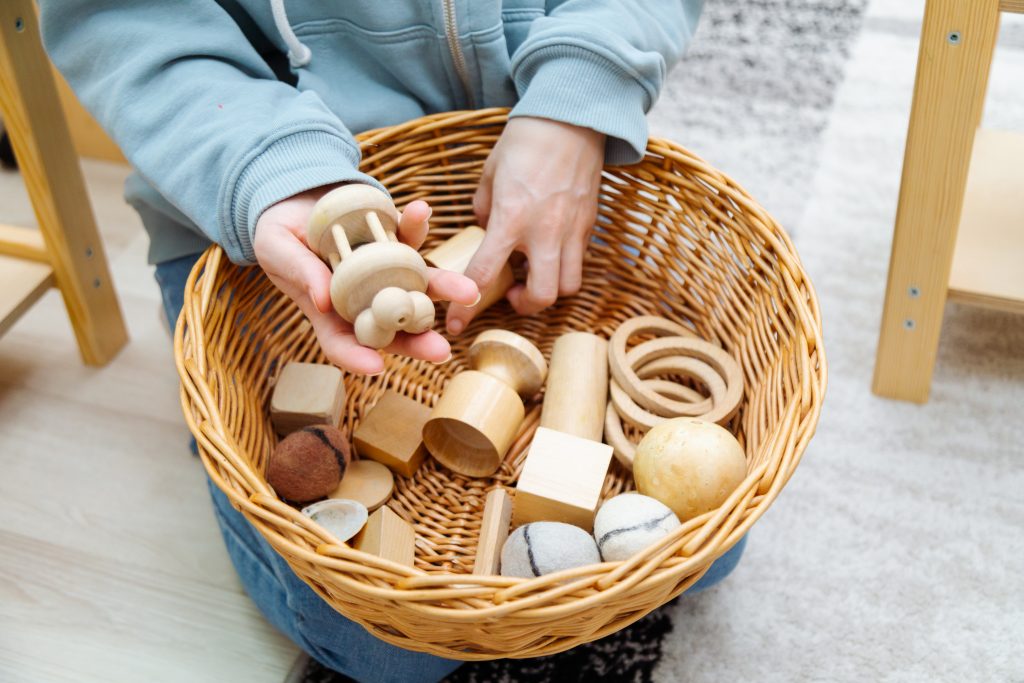 Kind greift in einen Korb voll mit Montessori Materialien